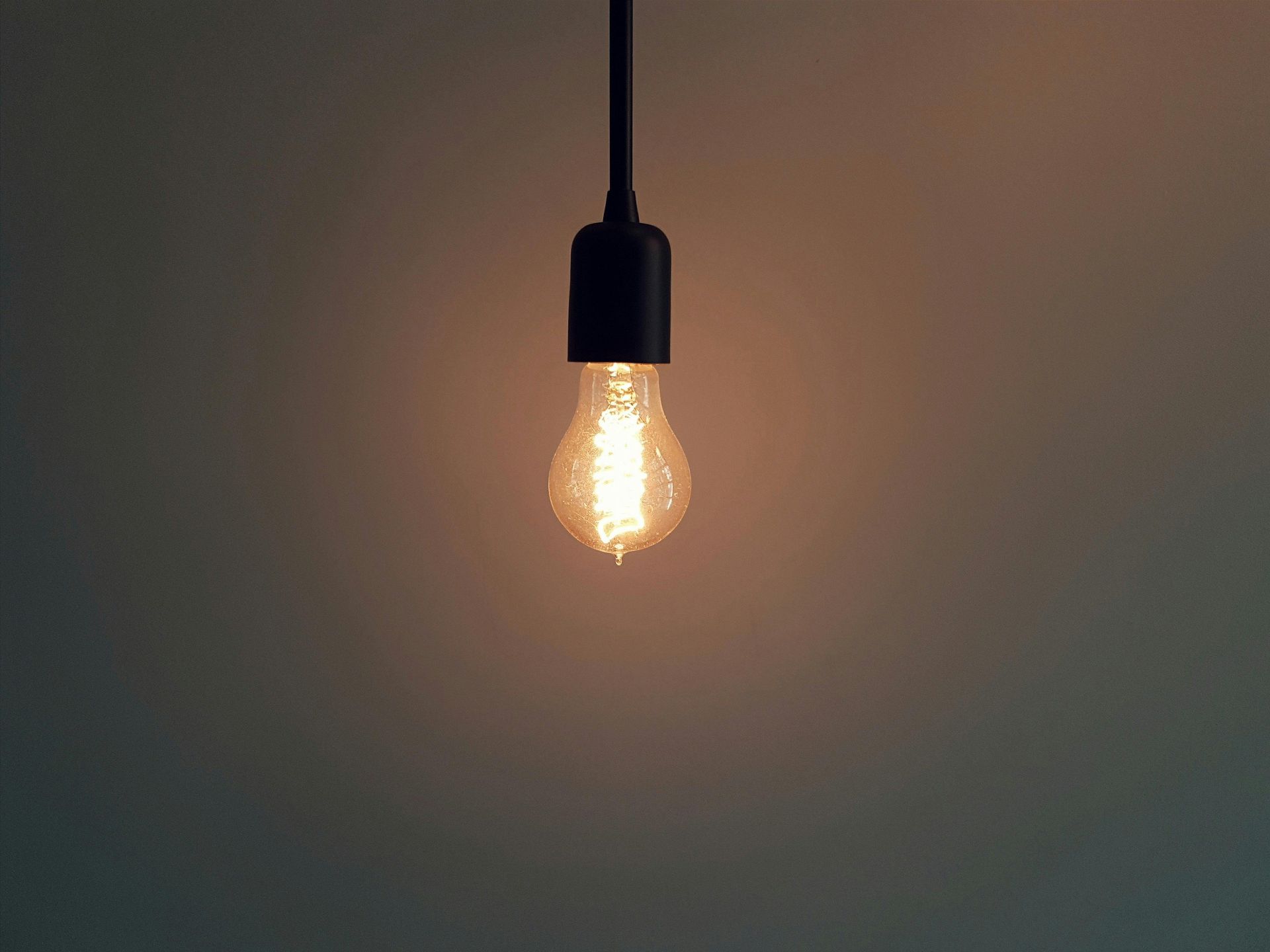 A glowing, vintage-style light bulb hangs against a dark, minimalist wall.