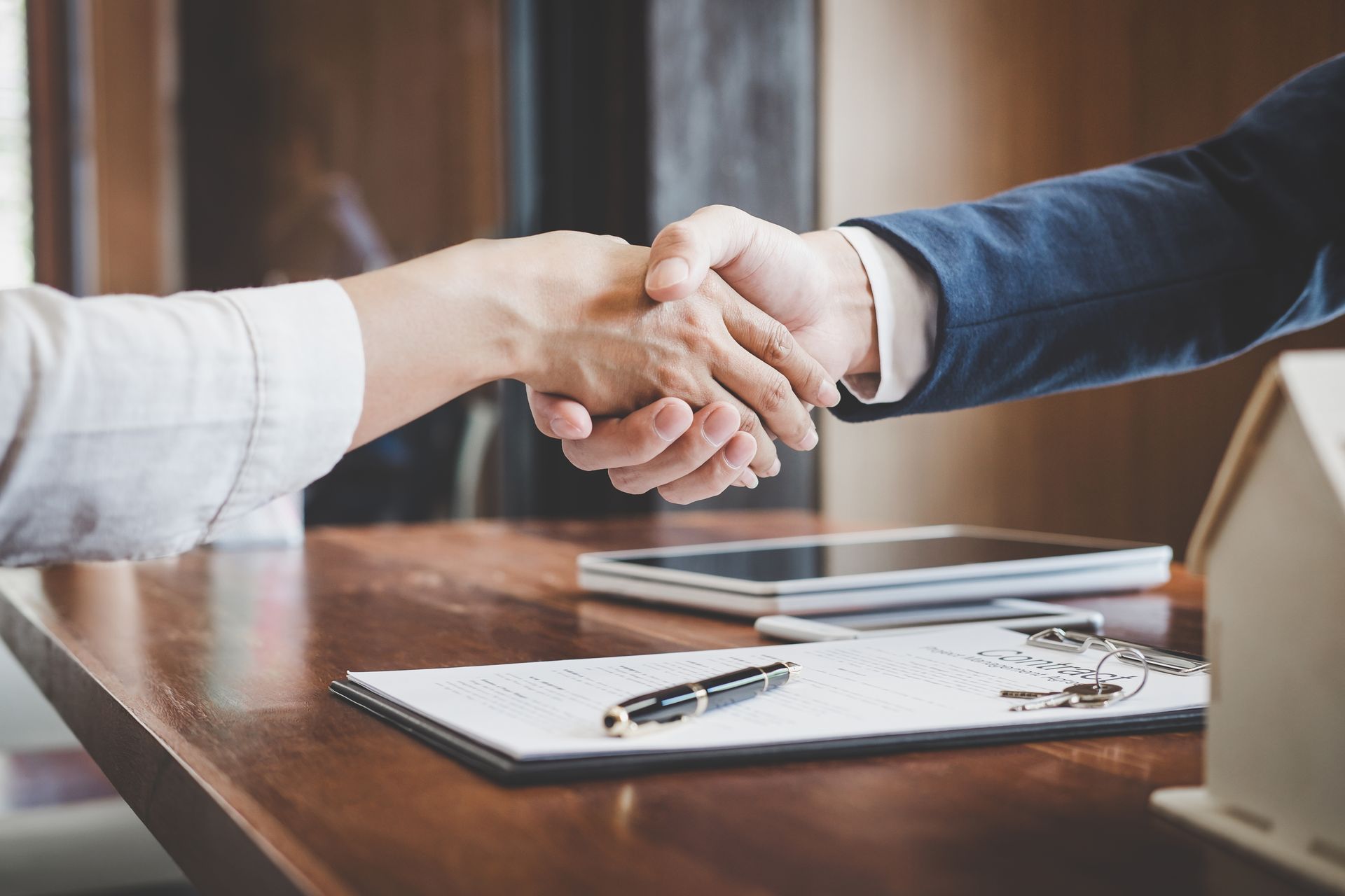 Two people shaking hands across a table with documents and eyeglasses in an office setting
