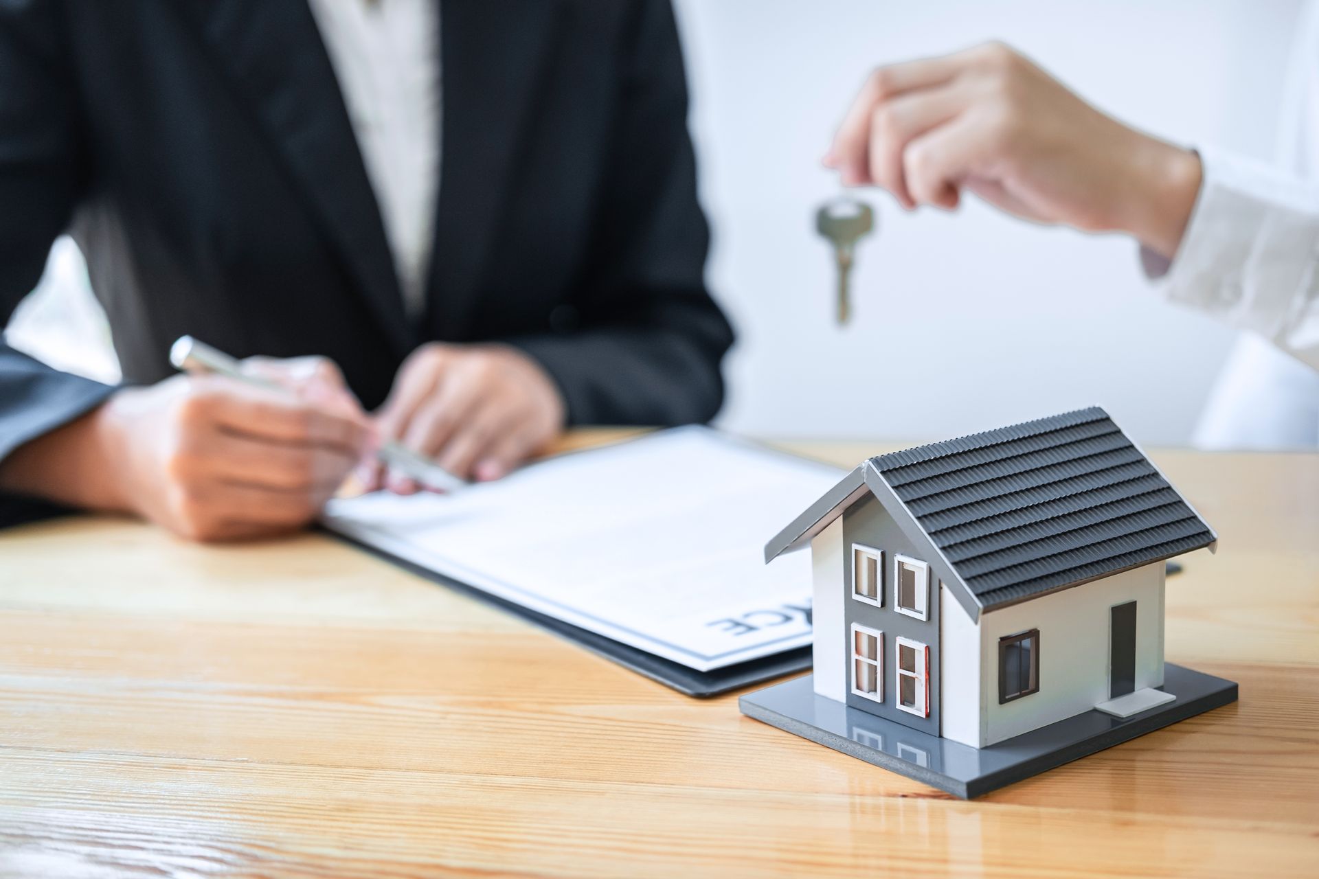 Handing over house keys during a real estate contract signing with a model house in the foreground