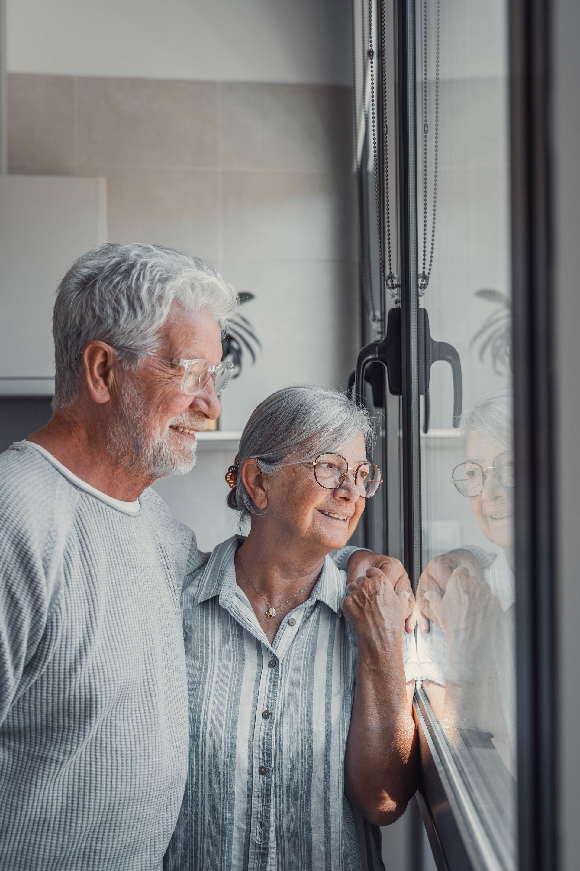 Two people standing by a window, looking outside and smiling softly.