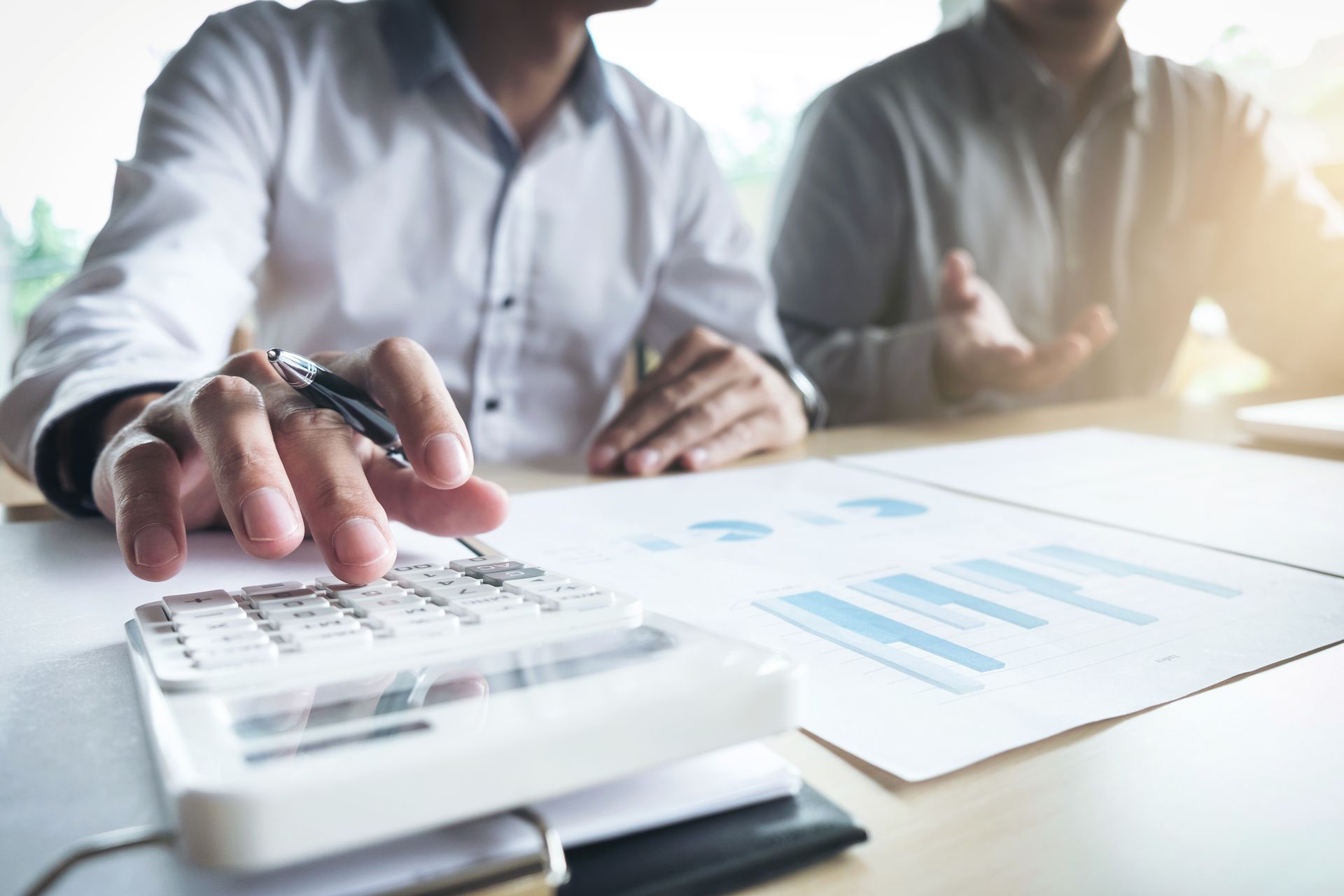 Hands using a calculator and reviewing financial charts on a bright office desk