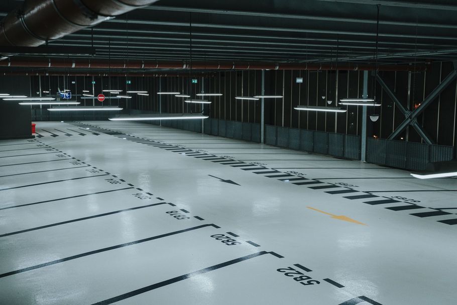 A symmetric view inside a parking garage with green floors, concrete pillars, and white painted directional arrows.