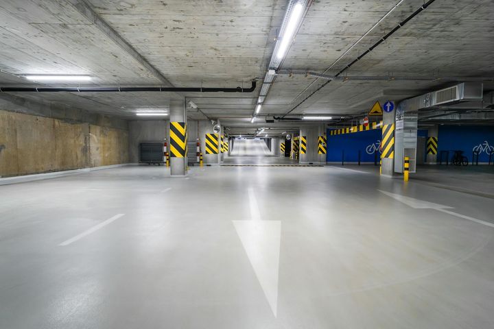 An empty underground parking garage with concrete ceilings, support pillars with yellow and black stripes, and white arrows.