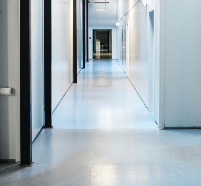 A paint roller applies white paint to a floor, with a blurred figure working in the background of a colorful warehouse.