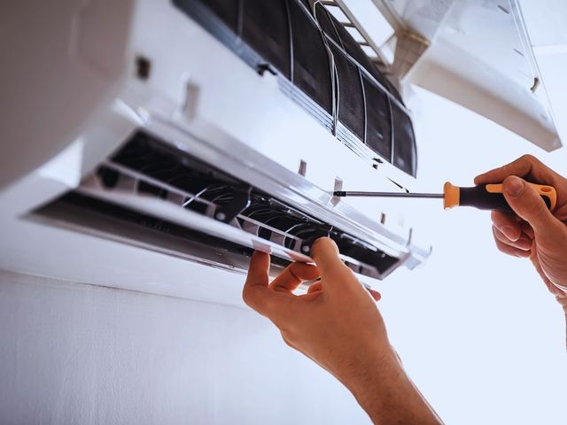 A person is repairing an air conditioner with a screwdriver.
