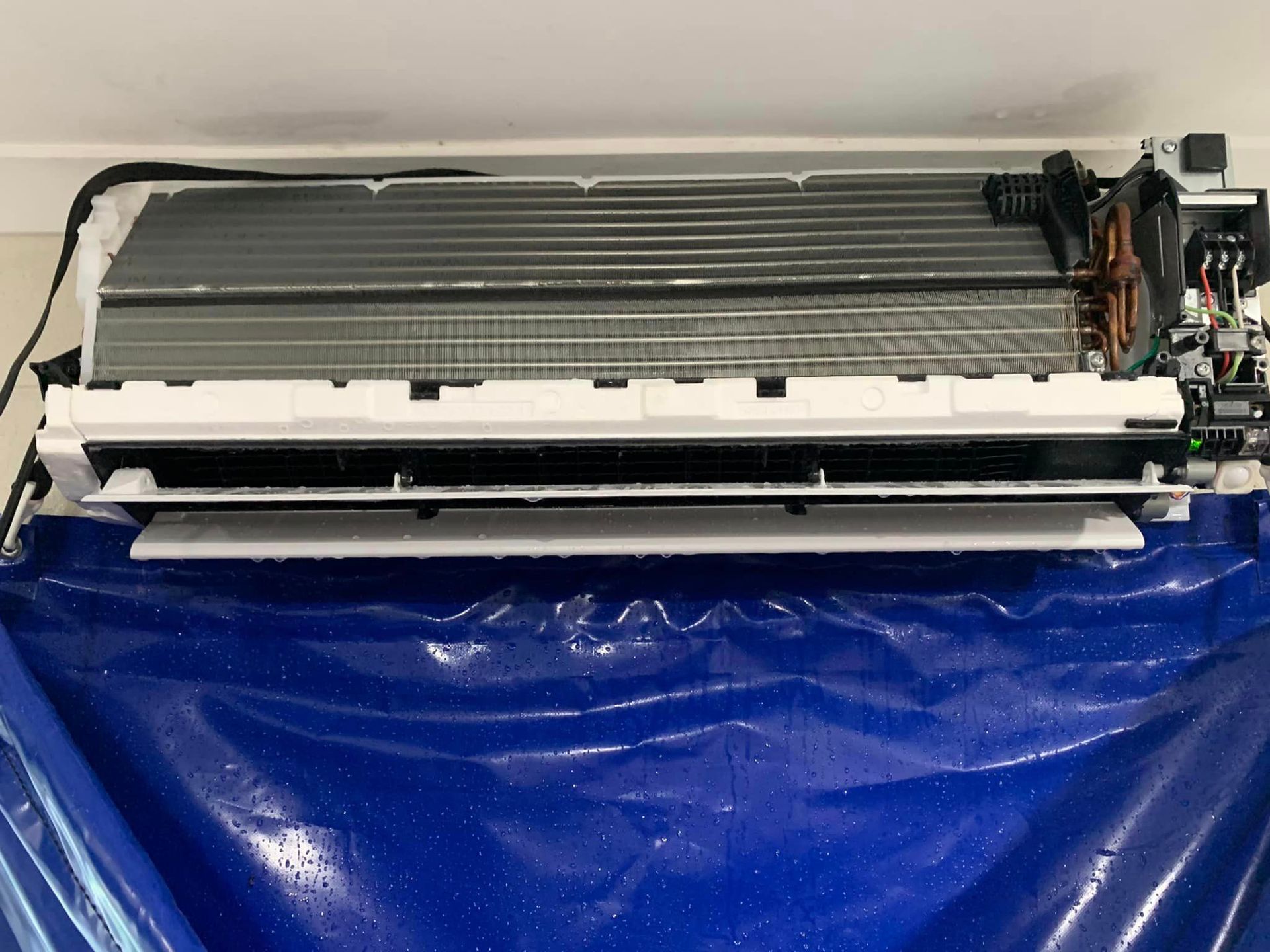 A white air conditioner is sitting on top of a blue plastic bag ready for hydro cleaning.