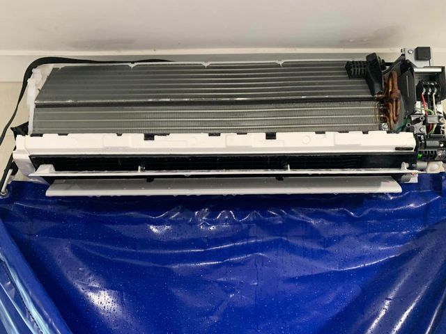 A white air conditioner is sitting on top of a blue plastic bag ready for a hydro clean