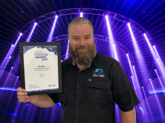 A man with a beard is holding a certificate in front of a stage.