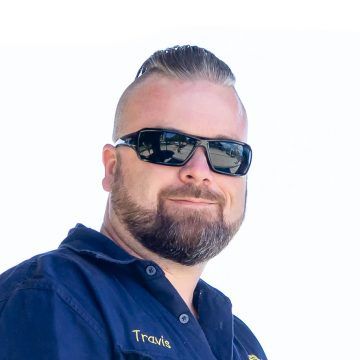 A man with a beard and sunglasses is wearing a blue shirt.