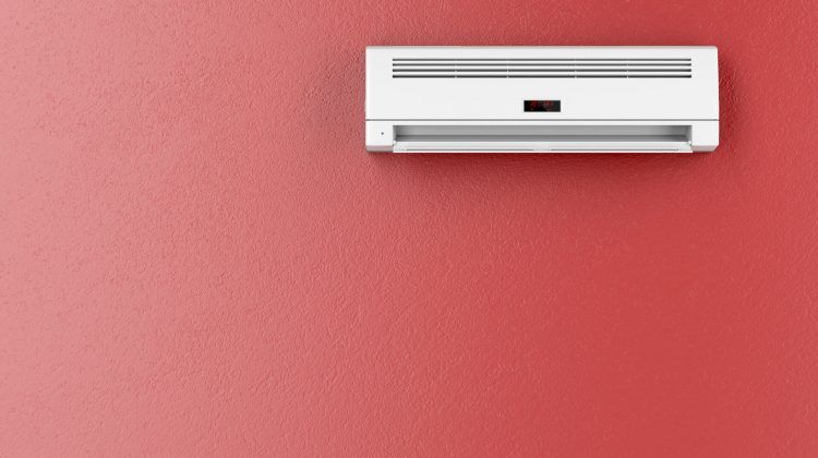A white air conditioner is hanging on a red wall.