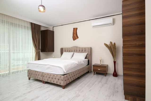 There is a large bed in the middle of the room with a white air conditioning unit above it on the wall.