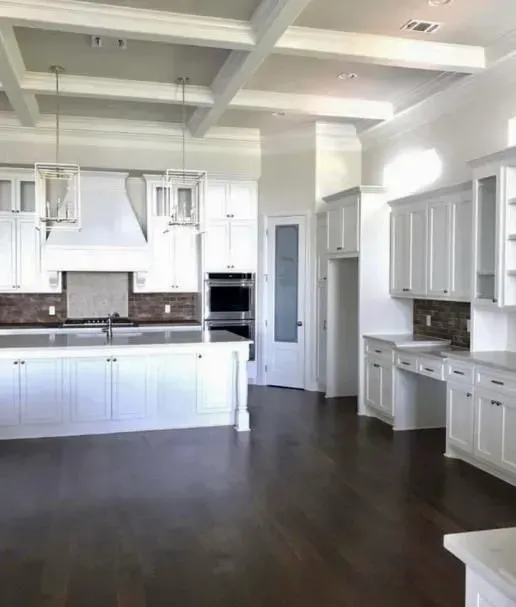 An empty kitchen with white cabinets and hardwood floors