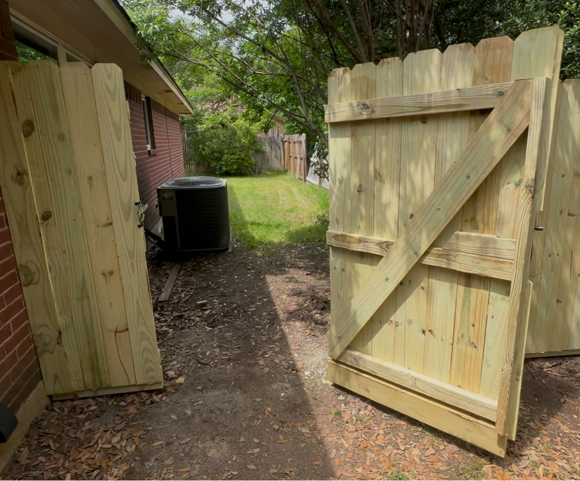 A wooden gate is open to a driveway in front of a house