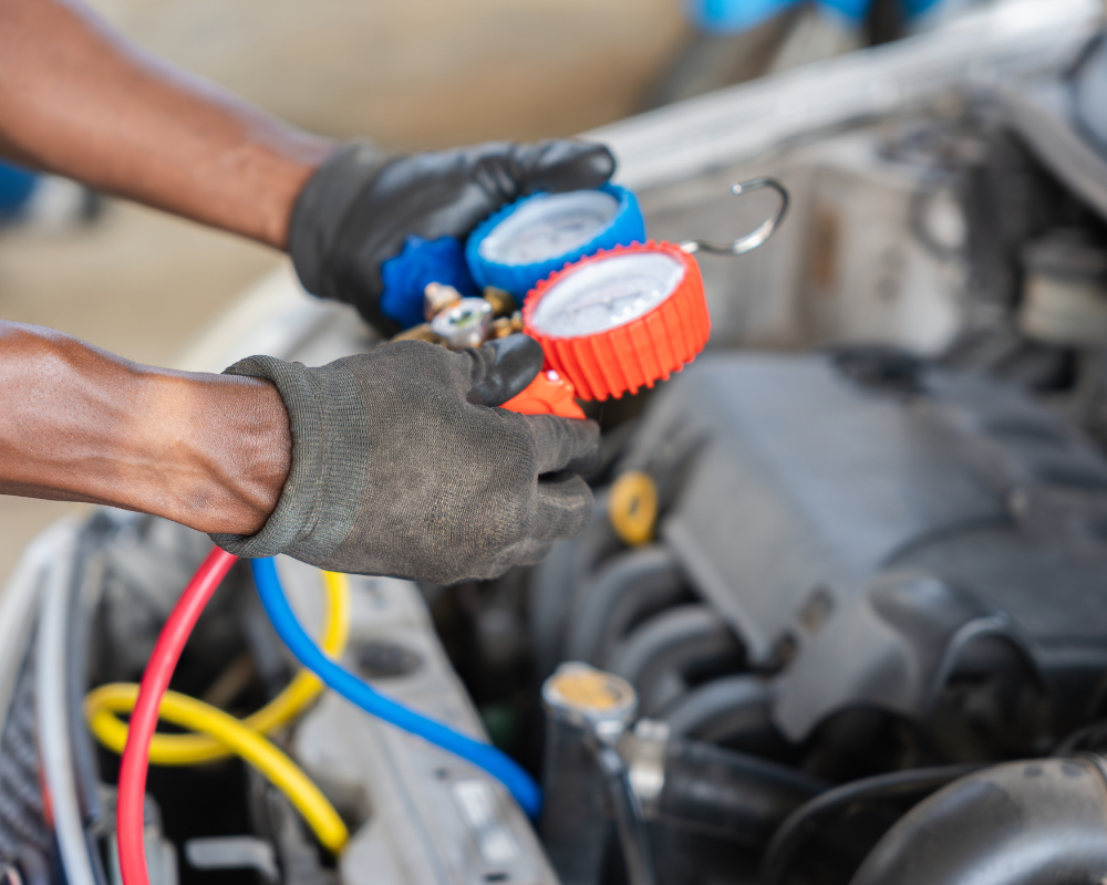 Mechanic using gauges to check a car's air conditioning system in an engine bay.