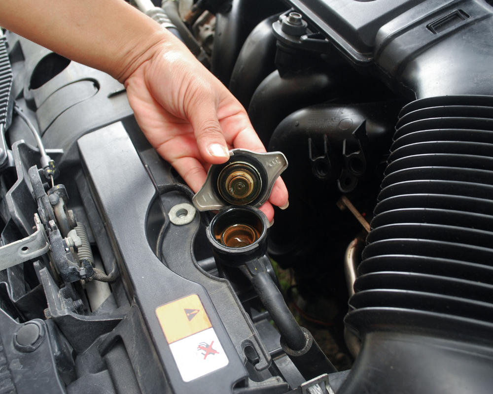 Hand opening car radiator cap, brown liquid visible.