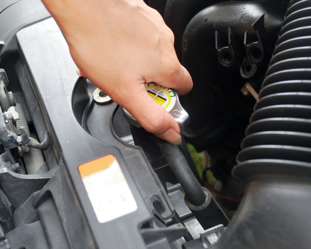 Hand opening a car radiator cap.