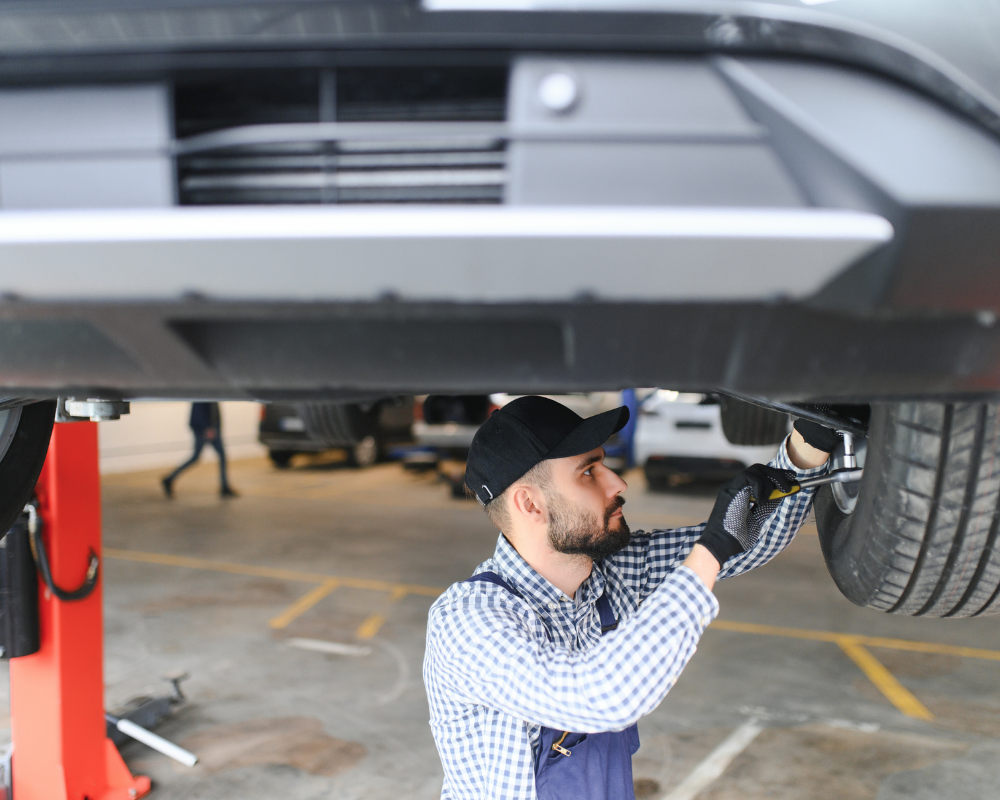 Mechanic working under a car, checking the wheel in a garage.