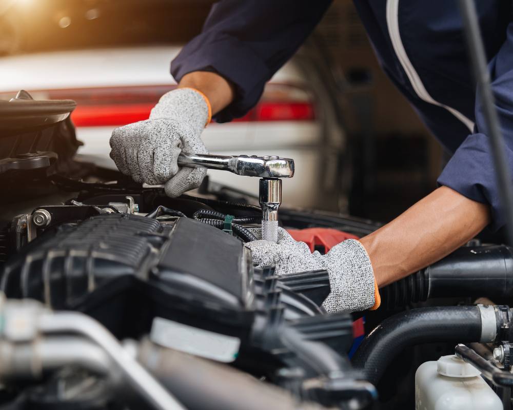 Mechanic in gloves using a wrench to work on a car engine.
