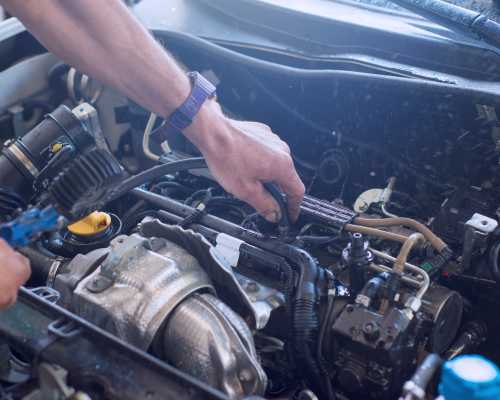Person cleaning a car engine with a spray bottle, details of the engine visible.