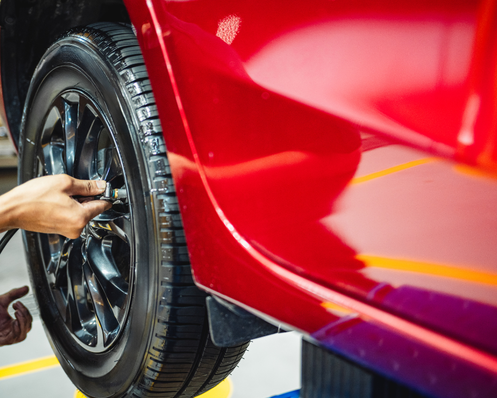 A person using a tool to work on a car's tire in a repair shop; red car.