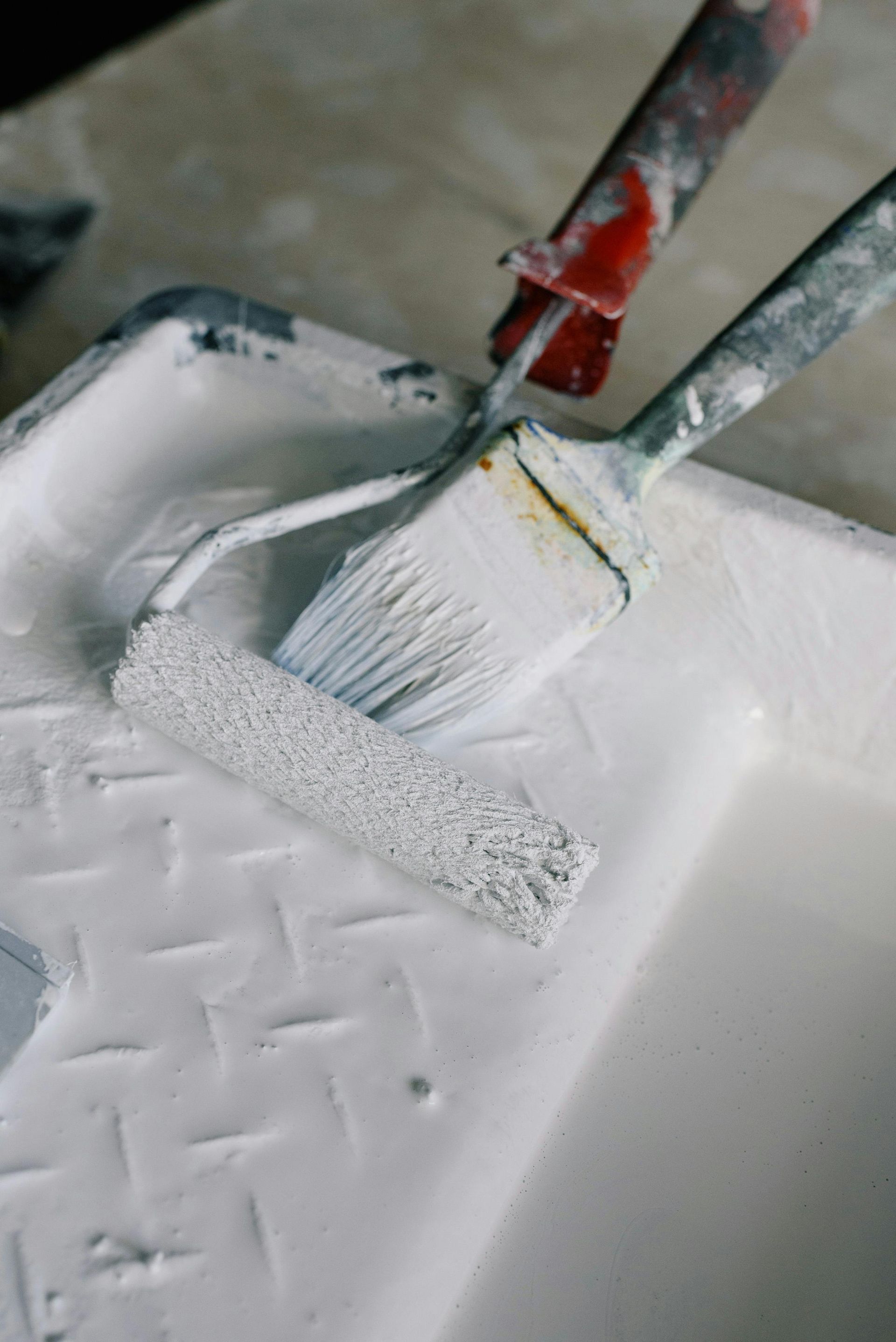 A paint roller and brush are sitting on top of a white paint tray.