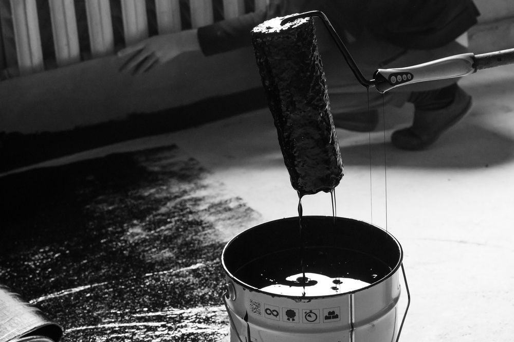 A black and white photo of a person pouring paint into a bucket