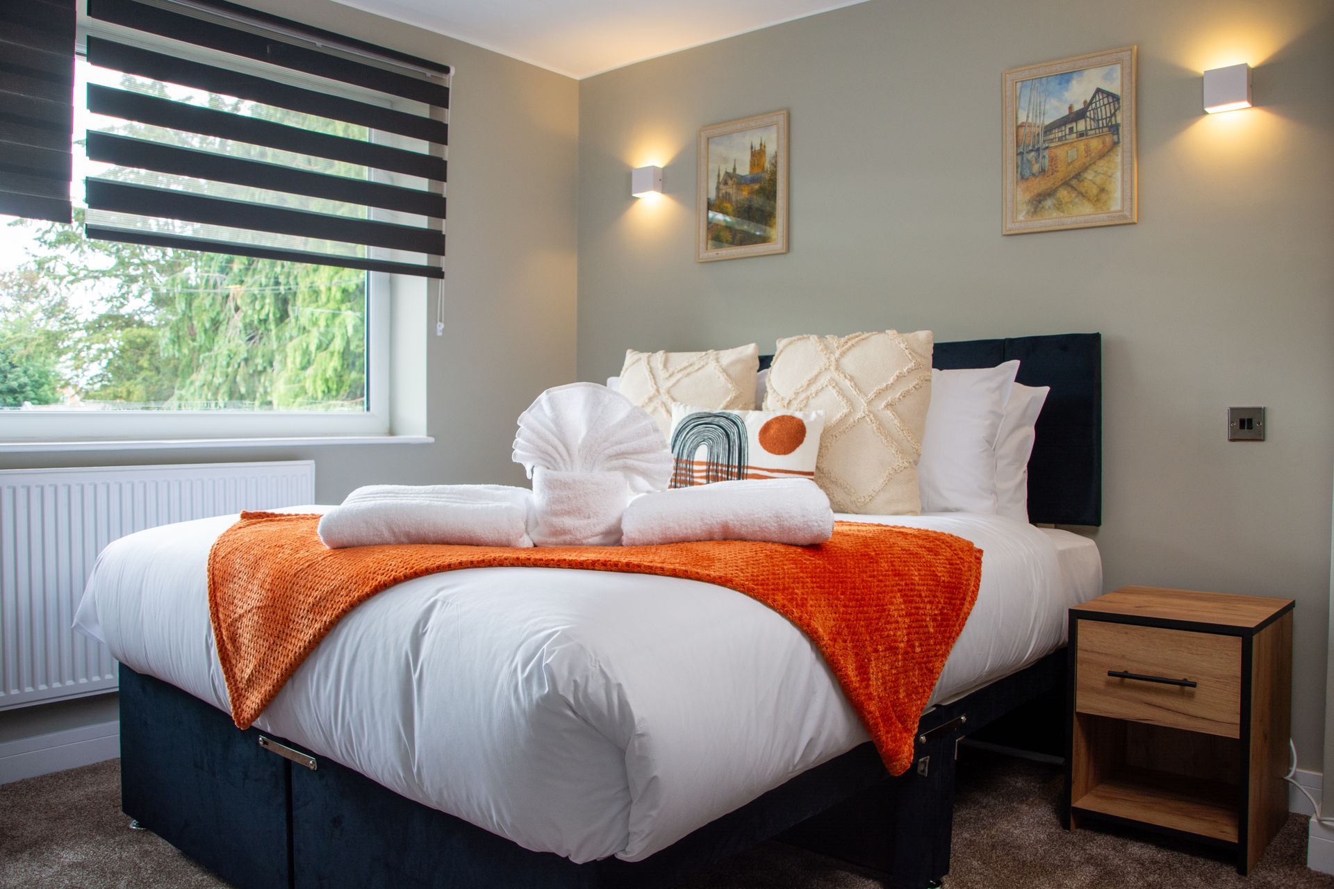 Modern bedroom with white bed, orange throw, striped blinds, and wall art by a window