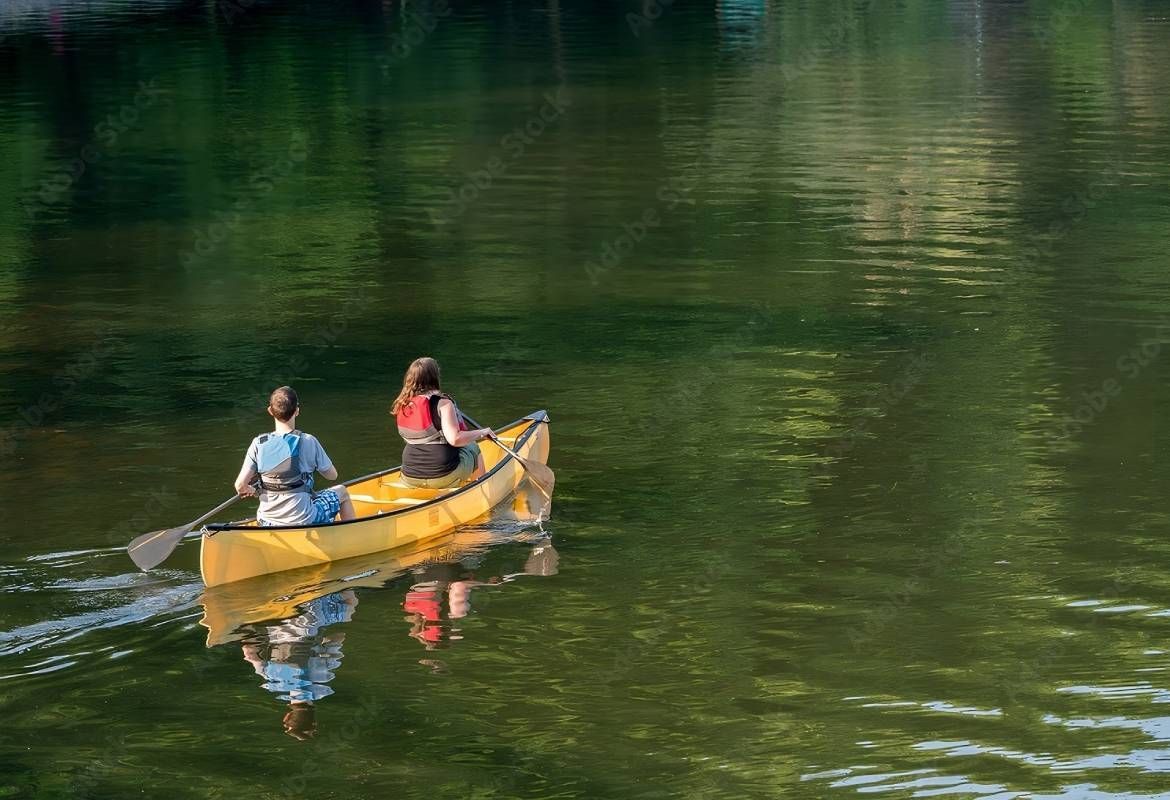 Couple paddling in yellow canoe on tree-lined lake at KY River Tours near Frankfort, KY