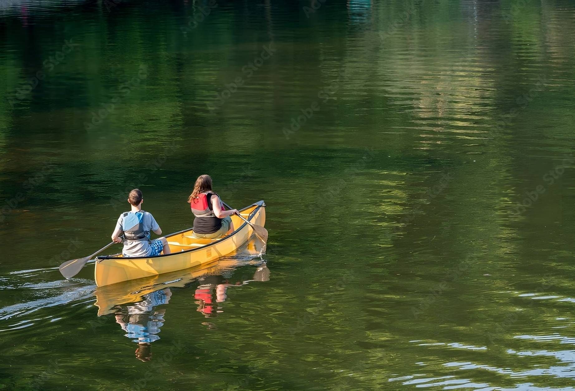 Couple paddling in yellow canoe on tree-lined lake at KY River Tours near Frankfort, KY