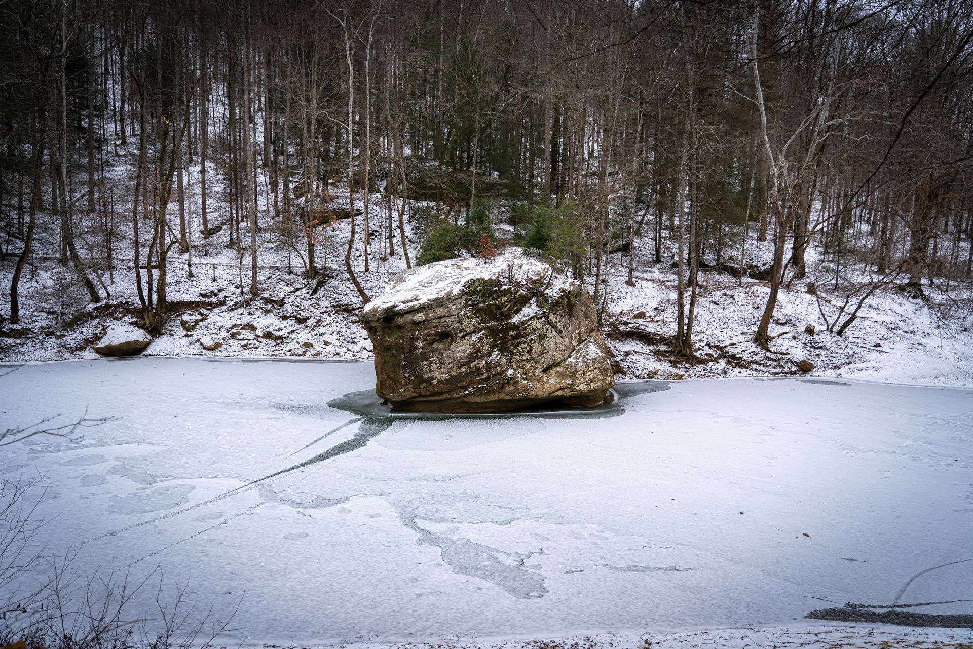 large rock in the middle of a frozen river surrounded by trees