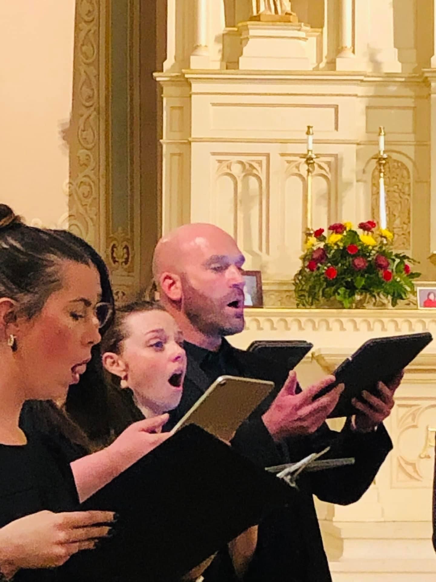 A group of people are singing in a church while holding tablets.