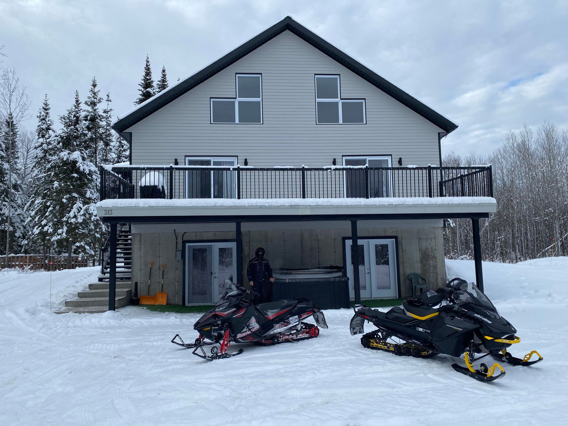 Deux motoneiges sont stationnées devant une maison dans la neige.