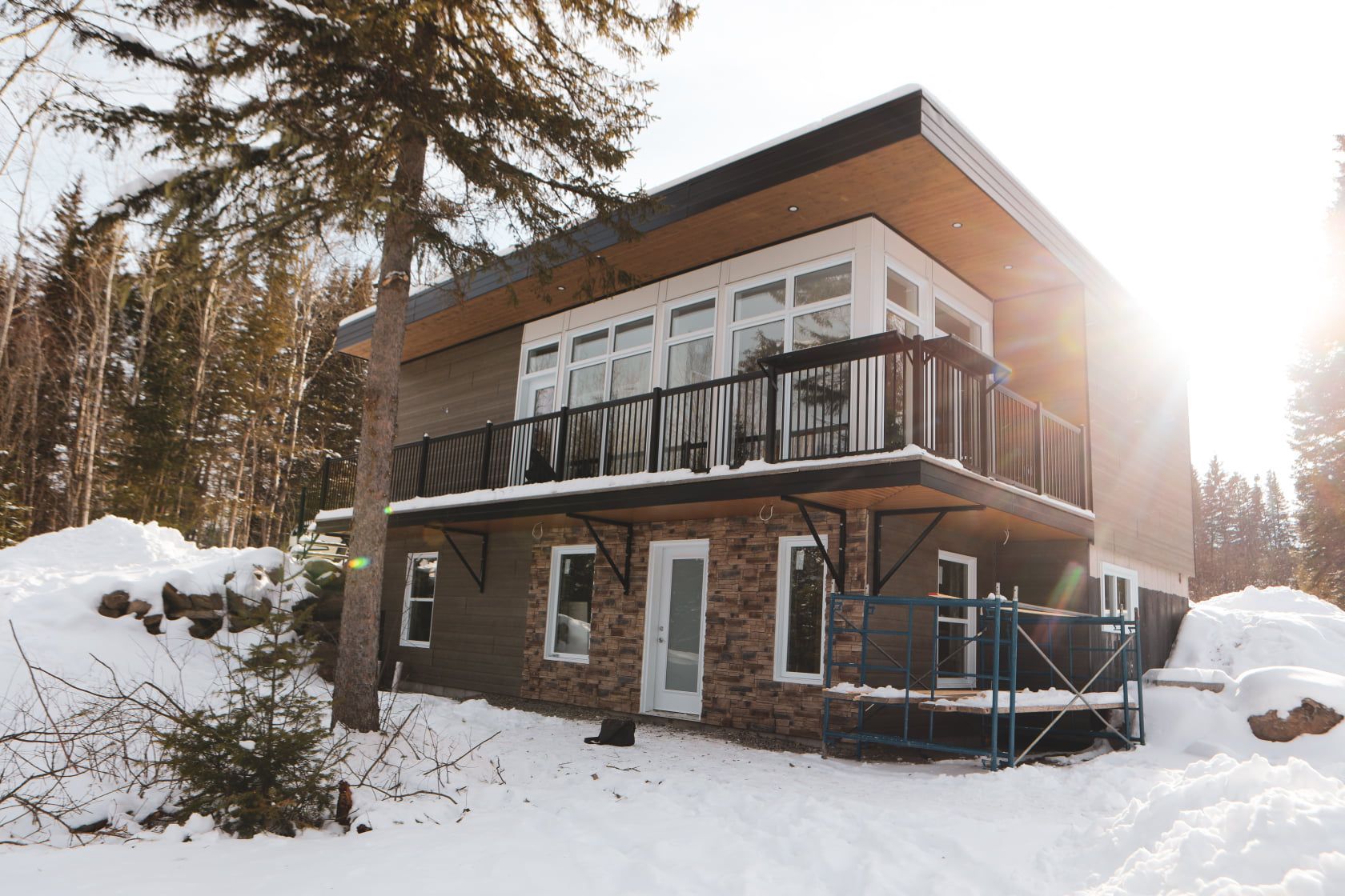 A house with a balcony is surrounded by snow and trees.