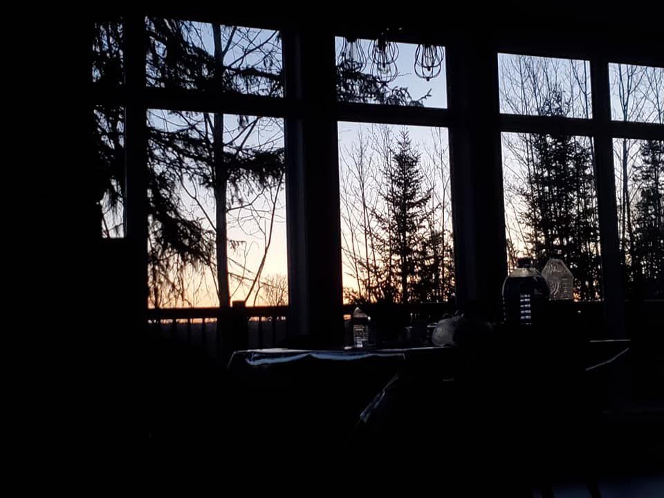 Un coucher de soleil est visible à travers les fenêtres d'une pièce sombre.