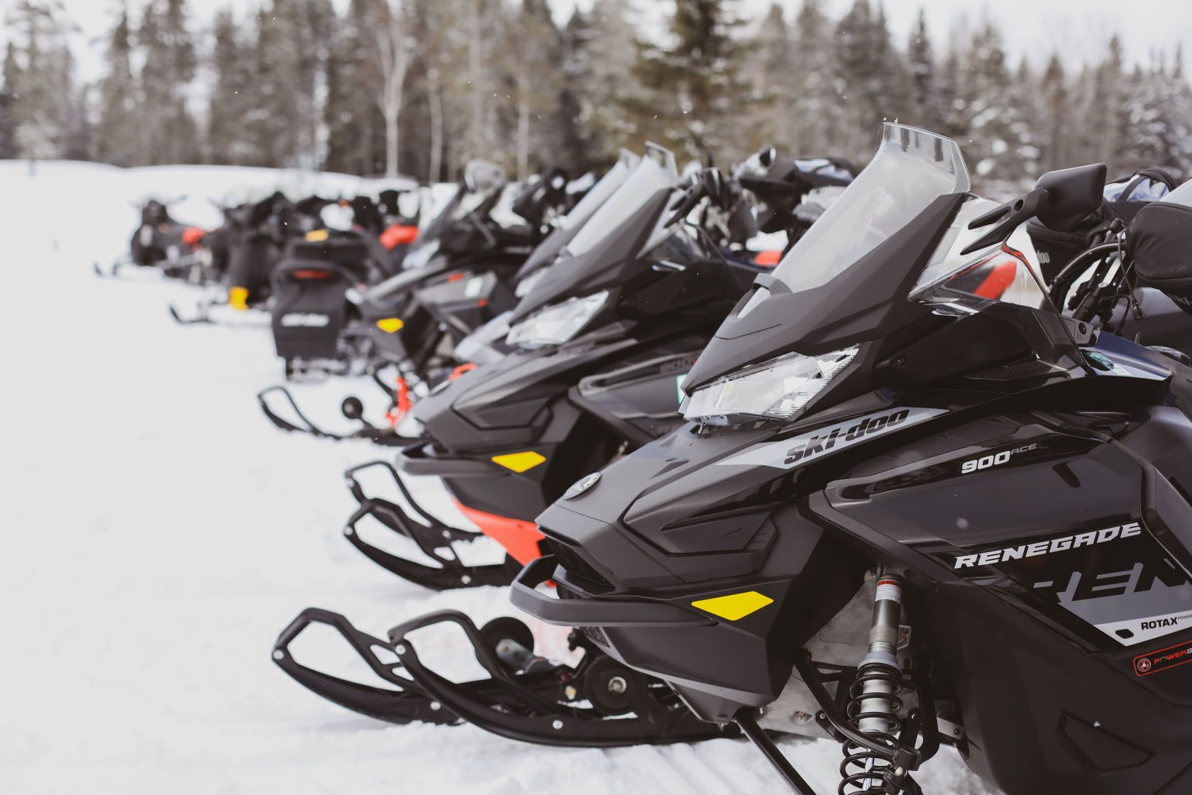 Une rangée de motoneiges est garée dans la neige.
