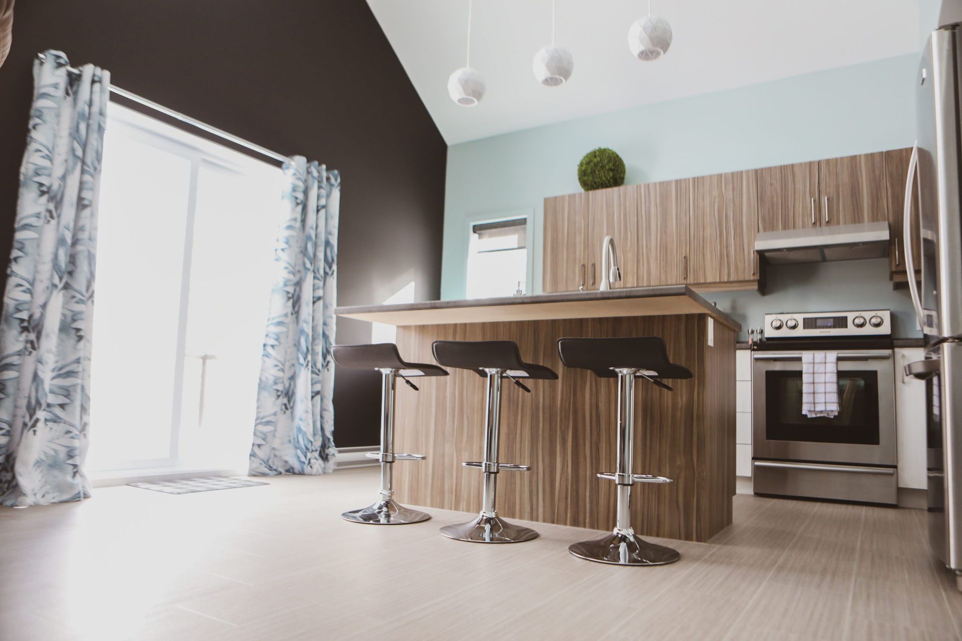 Une cuisine avec des tabourets, une cuisinière, un réfrigérateur et une fenêtre.