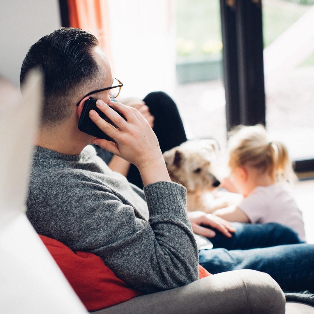 father looking at his dog and daughter while on phone