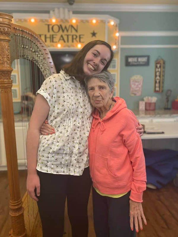 Two women are posing for a picture in front of a harp.