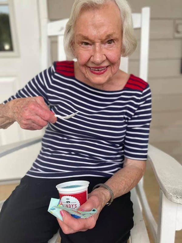 An elderly woman is sitting in a rocking chair eating ice cream with a spoon.
