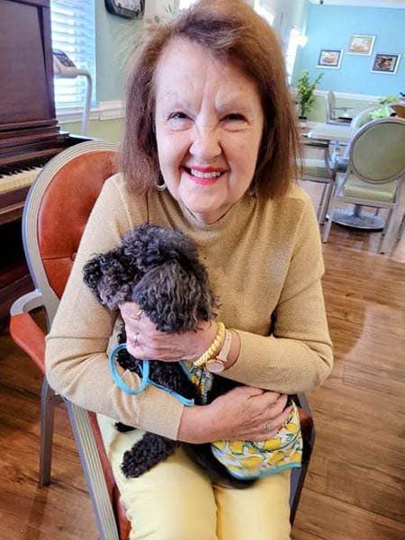 An elderly woman is sitting in a chair holding a small black dog.