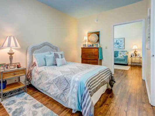 A bedroom with a bed , nightstand , dresser and lamp.