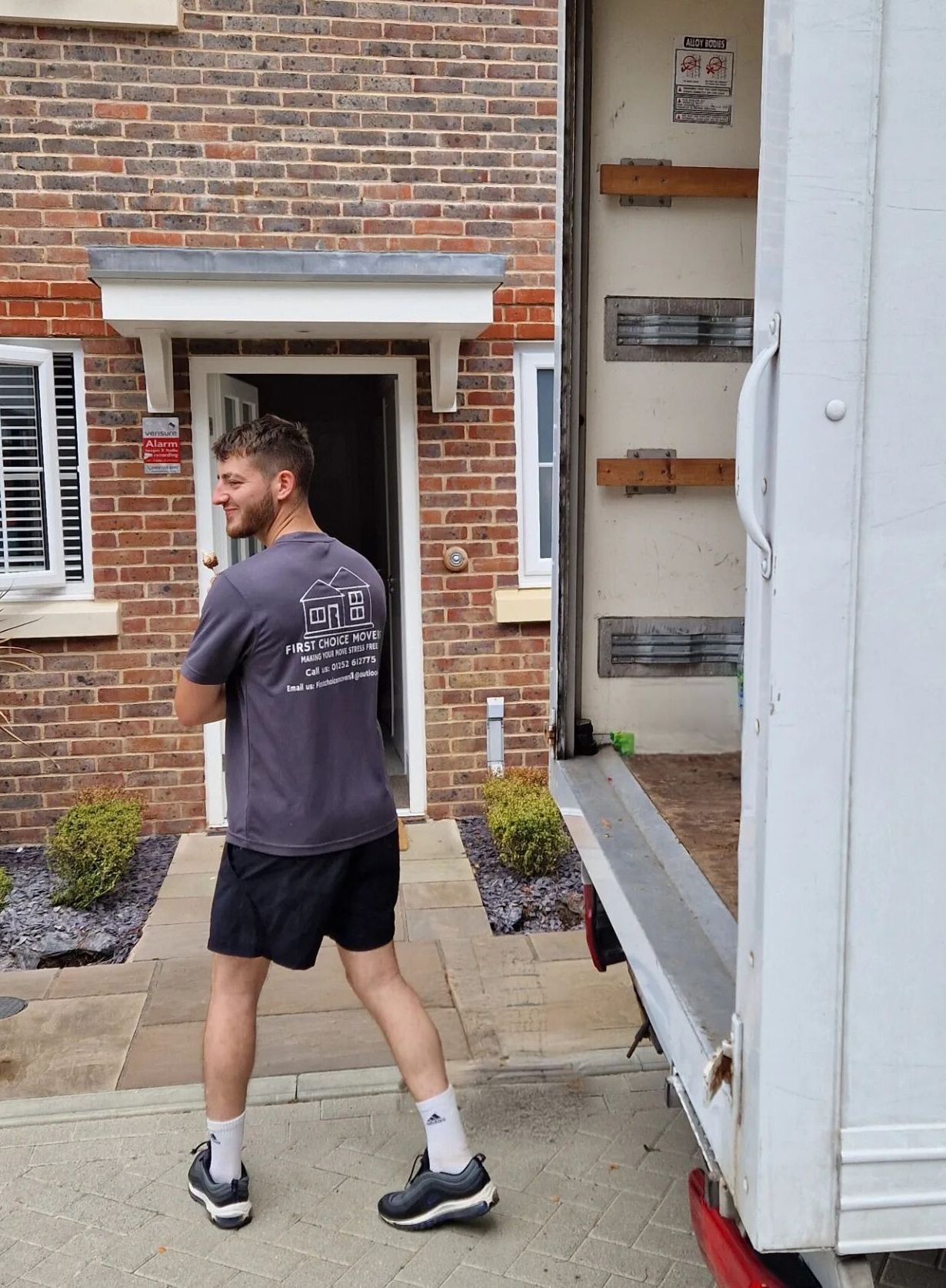 A man is standing in front of a white truck in front of a brick house.