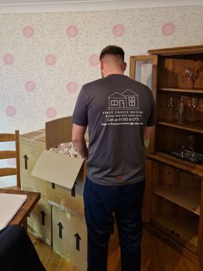 A man wearing a branded first choice movers t-shirt packing a box