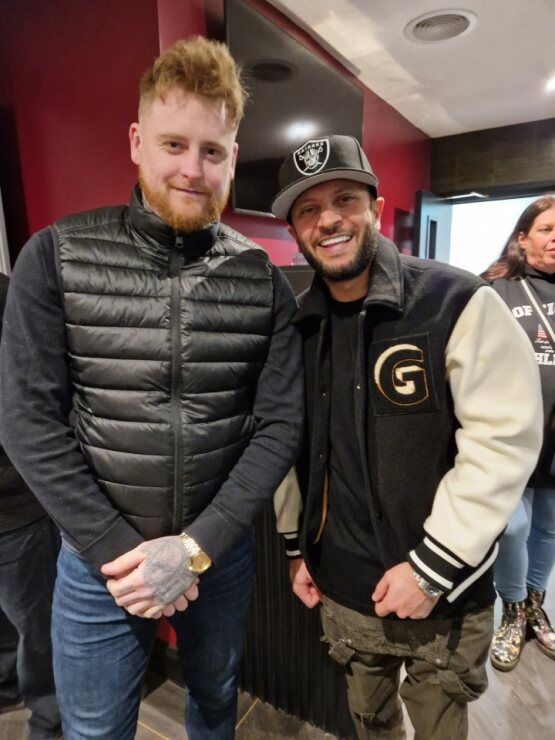 Two men are posing for a picture and one has a letter g on his jacket