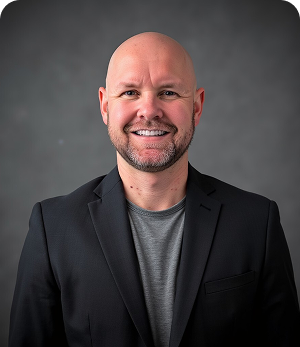 A bald man with a beard is wearing a suit and smiling.