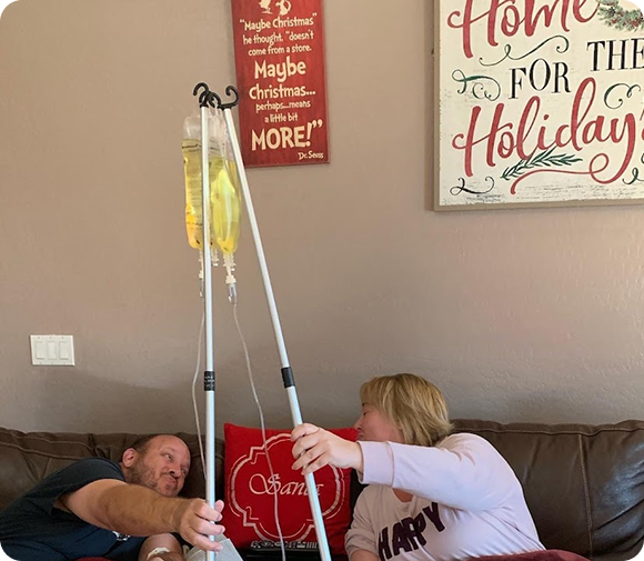 A man and woman are sitting on a couch with a sign that says home for the holidays