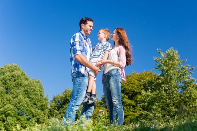Three people standing together in a sunny grassy park under a blue sky