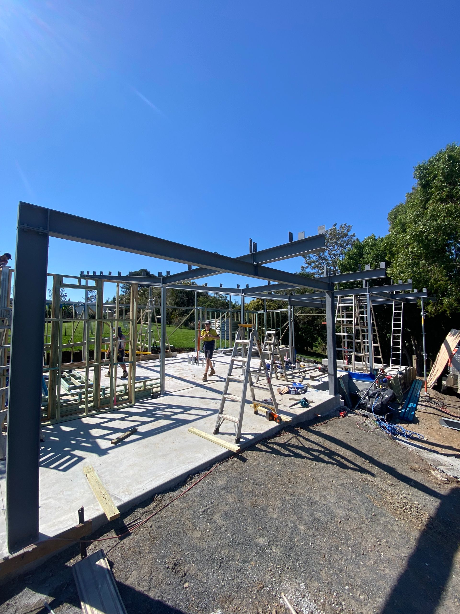 Construction site with steel frame structure and workers, sunny day.