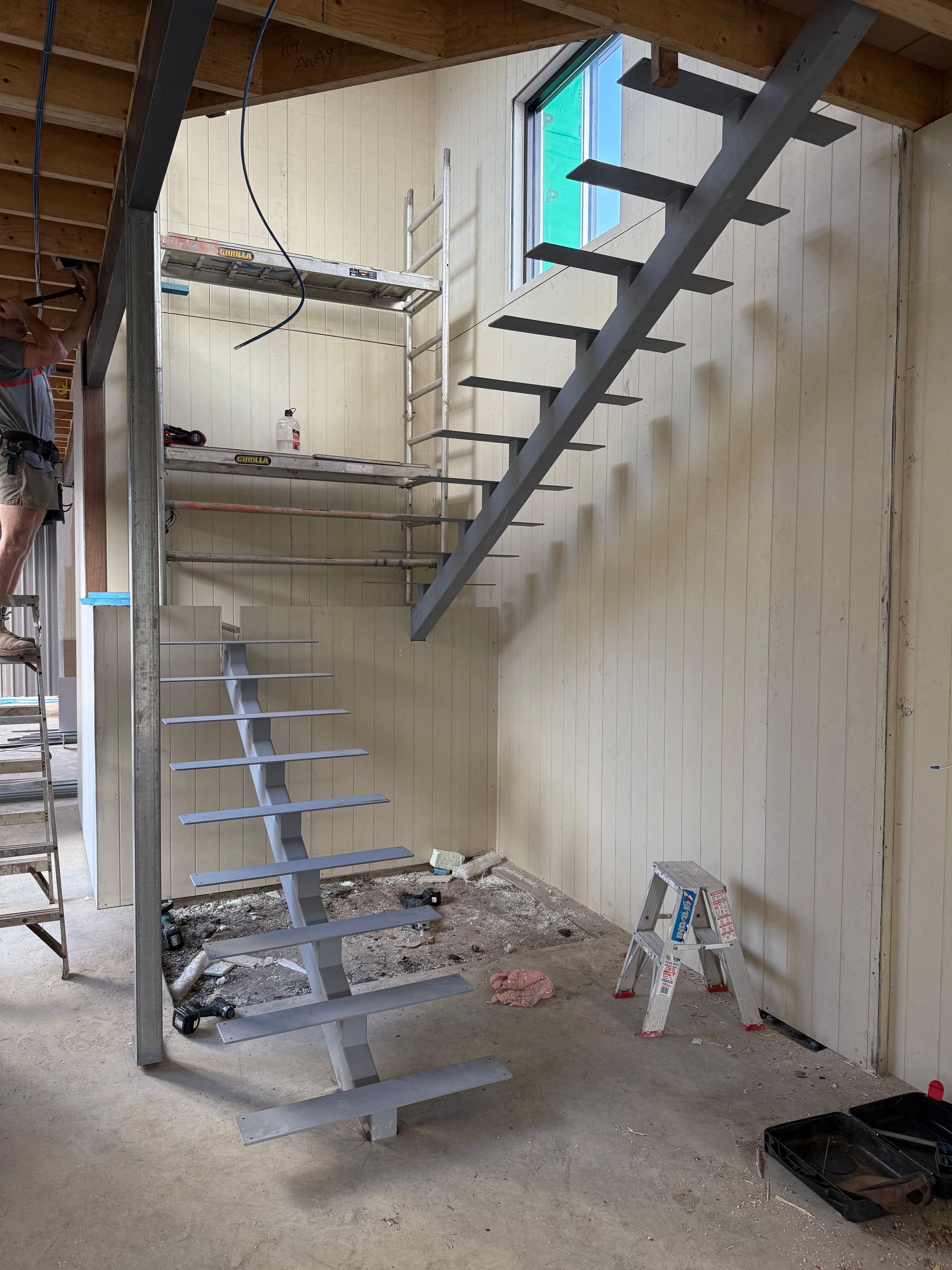 Metal staircase under construction in a room with light-colored walls and a window.