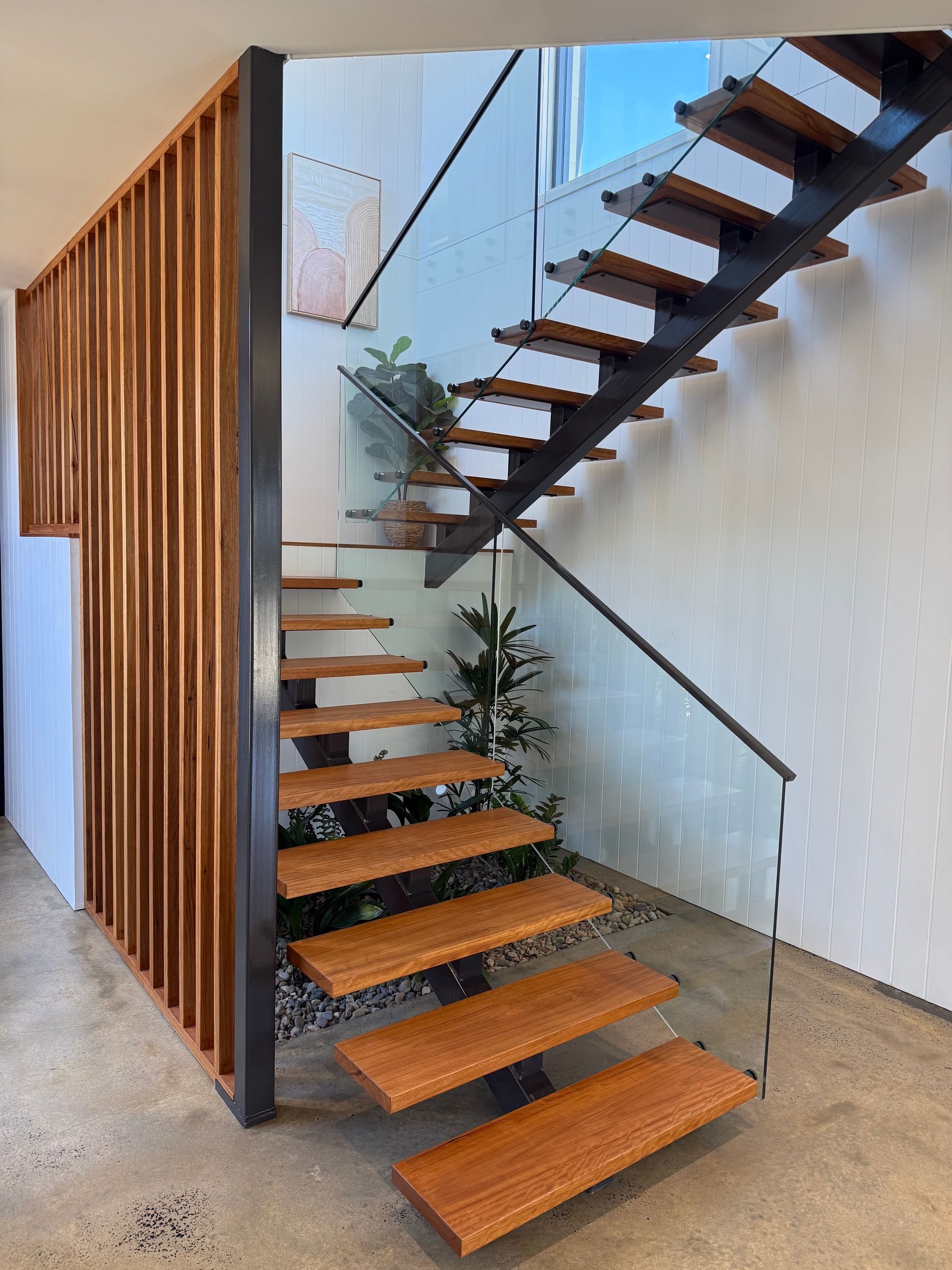 Wooden floating staircase with glass railing and decorative wood paneling in a modern interior.